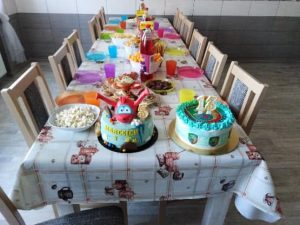 Stół urodzinowy na którym stoją słodycze talerzyki kubeczki i dwa torty