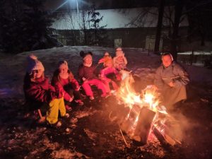 Dzieci wraz z Siostrą Zakonną siedzą w koło ogniska