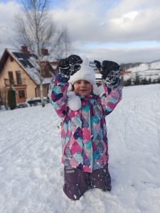 Dziewczynka klęcząca na śniegu i unosząca ręce do góry