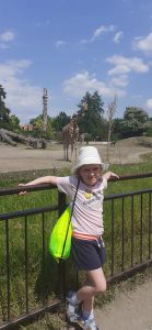 Dziewczynka a za nią stoi żyrafa