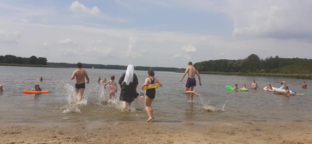 Grupka dzieci razem z Siostrą zakonną biegną do wody