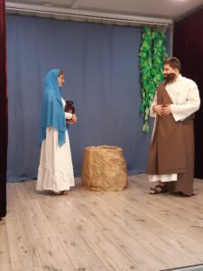 Maryja stoi obok studni i rozmawia ze stojącym na przeciw nim Józefem
