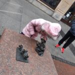 Dziewczynka w rózowej kurtce schyla się do krasnoludków które spotkała we Wrocławiu