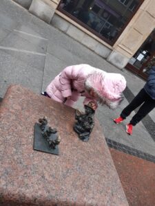 Dziewczynka w rózowej kurtce schyla się do krasnoludków które spotkała we Wrocławiu