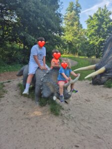 trójka dzieci siedząca na dinozaurze naturalnych rozmiarów.